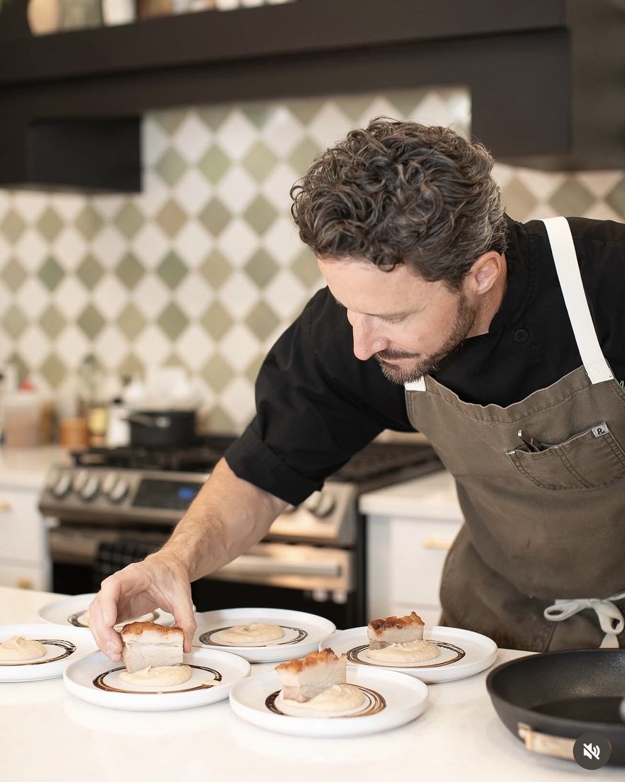 Jason plating pork belly over a swipe of puree in a bright kitchen, five plates lined up along the counter.