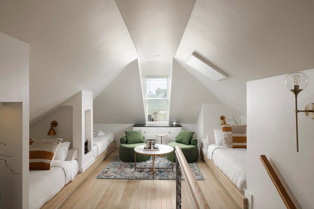 The Loft: a long room under the eaves with beds along both sides, two green armchairs, a skylight and a dormer window.