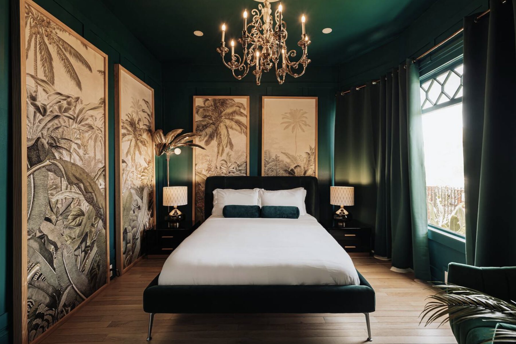 A bedroom at The Jade Manor: deep green walls, a crystal chandelier, botanical palm panels and a velvet bed.
