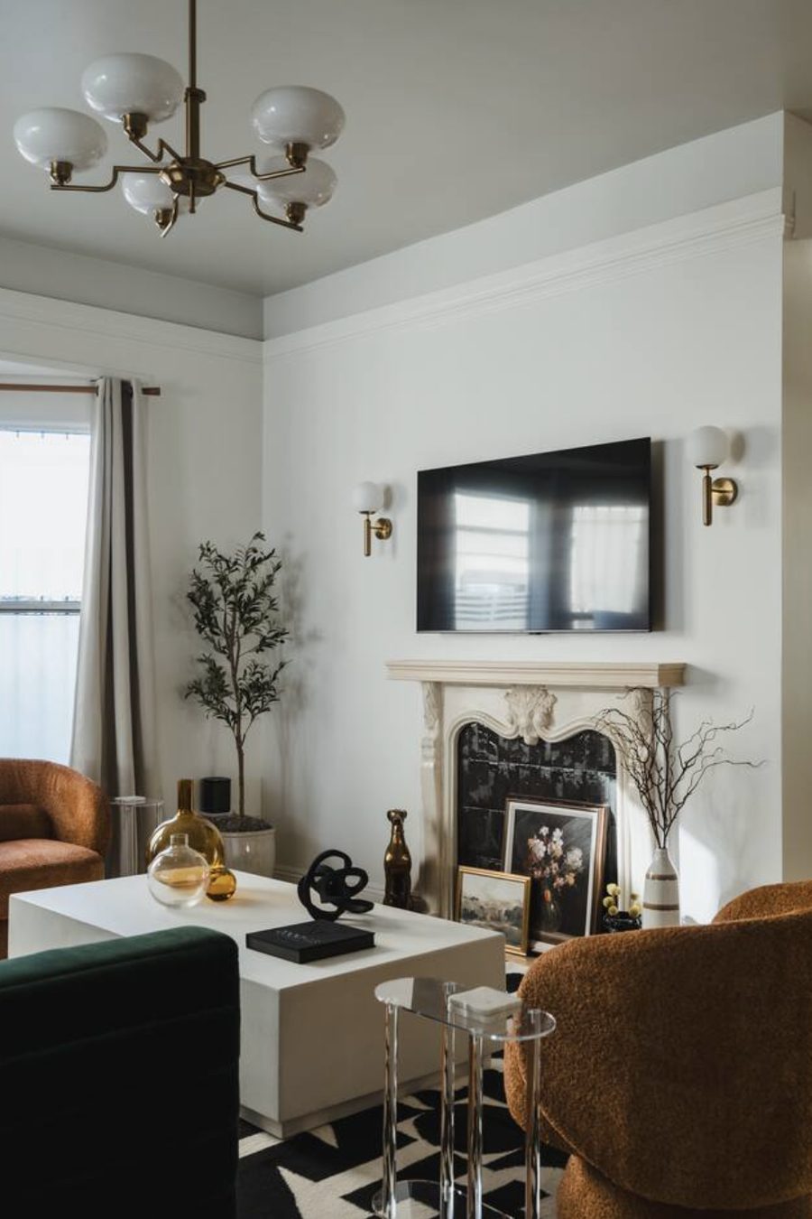 The living room at The Jade Manor: a carved marble fireplace with a black tiled hearth, brass chandelier and sconces, rust boucle armchairs and a green velvet sofa.