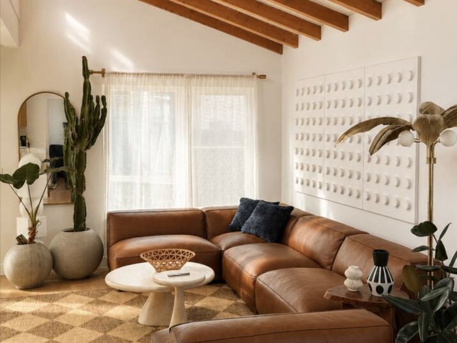 A white living room at Casa Coolangatta with exposed timber beams, a tall cactus and a tan leather sectional.