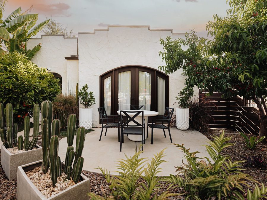 Kirra Villa at dusk: a white Spanish bungalow with arched timber doors, framed by cacti and ferns.