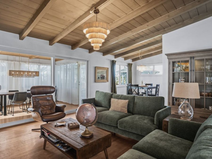 The Palms: an open living room under a wood plank beamed ceiling, with green sofas and sliding doors to a dining area.