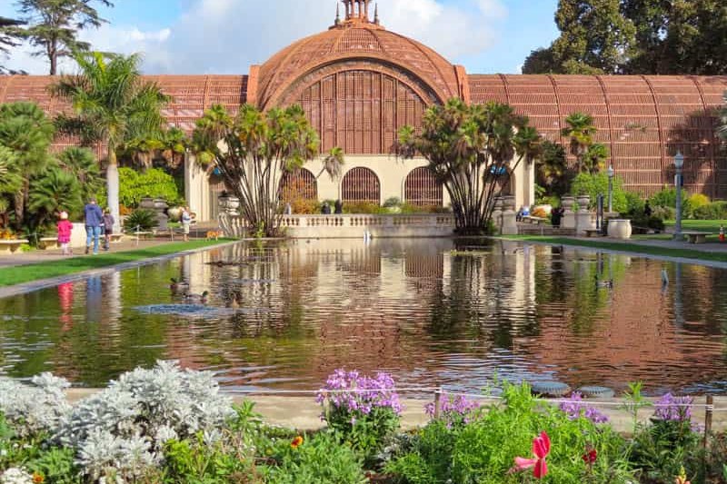 The Botanical Building in Balboa Park: a domed lath house of redwood slats reflected in the lily pond, with palms and flowerbeds around it.