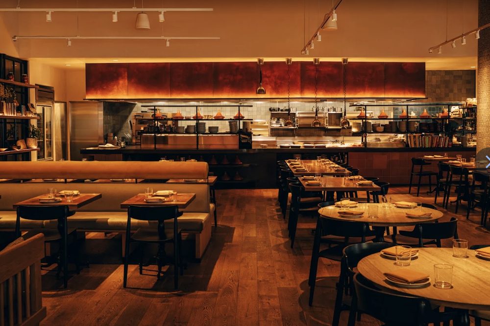 The dining room at Callie: warm low light, an open kitchen along the back wall, timber tables and long banquettes.