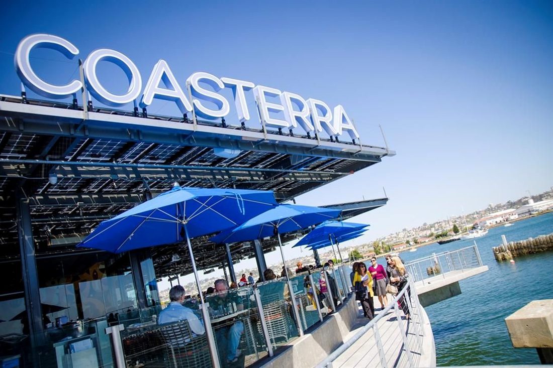 Coasterra on Harbor Island: the name in white letters above a solar canopy, blue umbrellas over the waterfront terrace and the bay beyond.