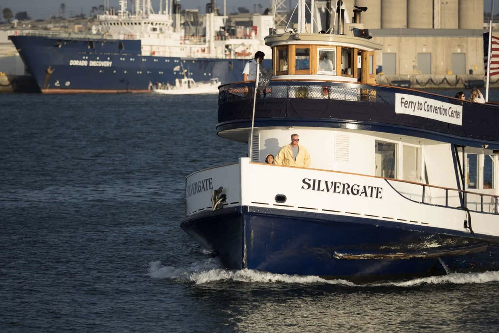 The Silvergate ferry crossing San Diego Bay in late afternoon light, a navy research ship moored behind it.