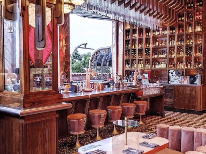 Inside Morning Glory: deco brass lamps, a wall of bottles, pink velvet stools and terrazzo floors.